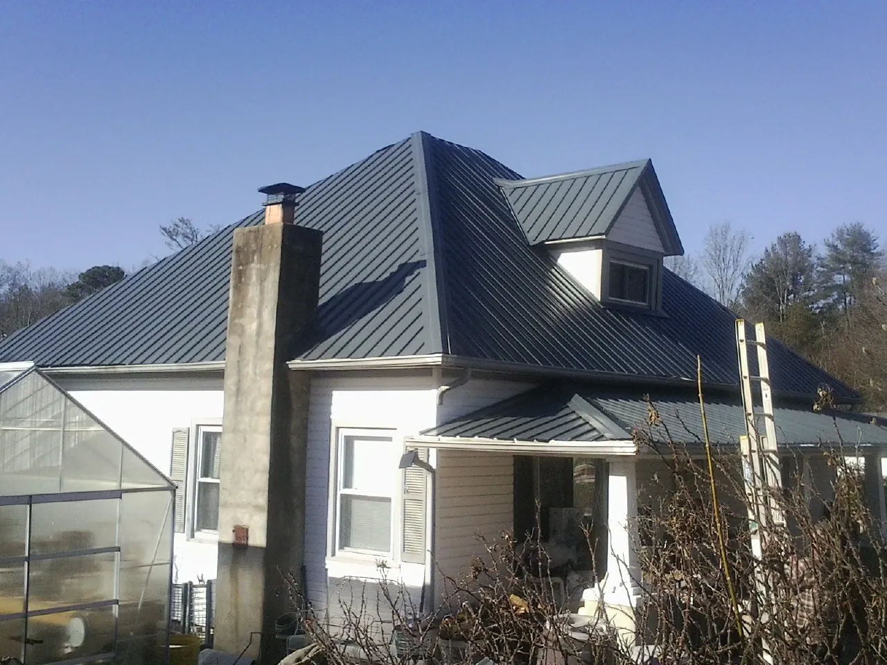 Dark blue standing seam metal roof on a white farmhouse with dormer — Slate & Tile Roof Repair by Roofing Brothers in Fort Mc Coy