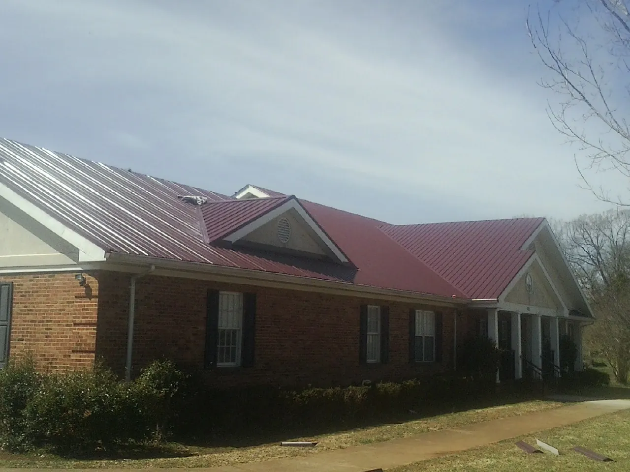 Red metal roof with gabled entries on a long brick building, from a Hail Damage Roof Repair job in Fort Mc Coy