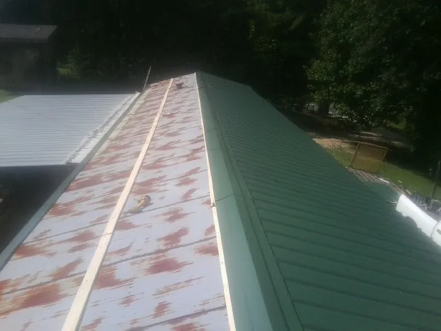 Old rusted panels beside newly installed green metal roofing — Wind Damage Roof Repair by Roofing Brothers in Fort Mc Coy
