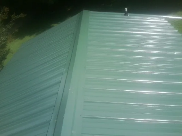 New green metal panels meeting at the ridge of a roof — Flat Roof Repair work by our crew in Fort Mc Coy