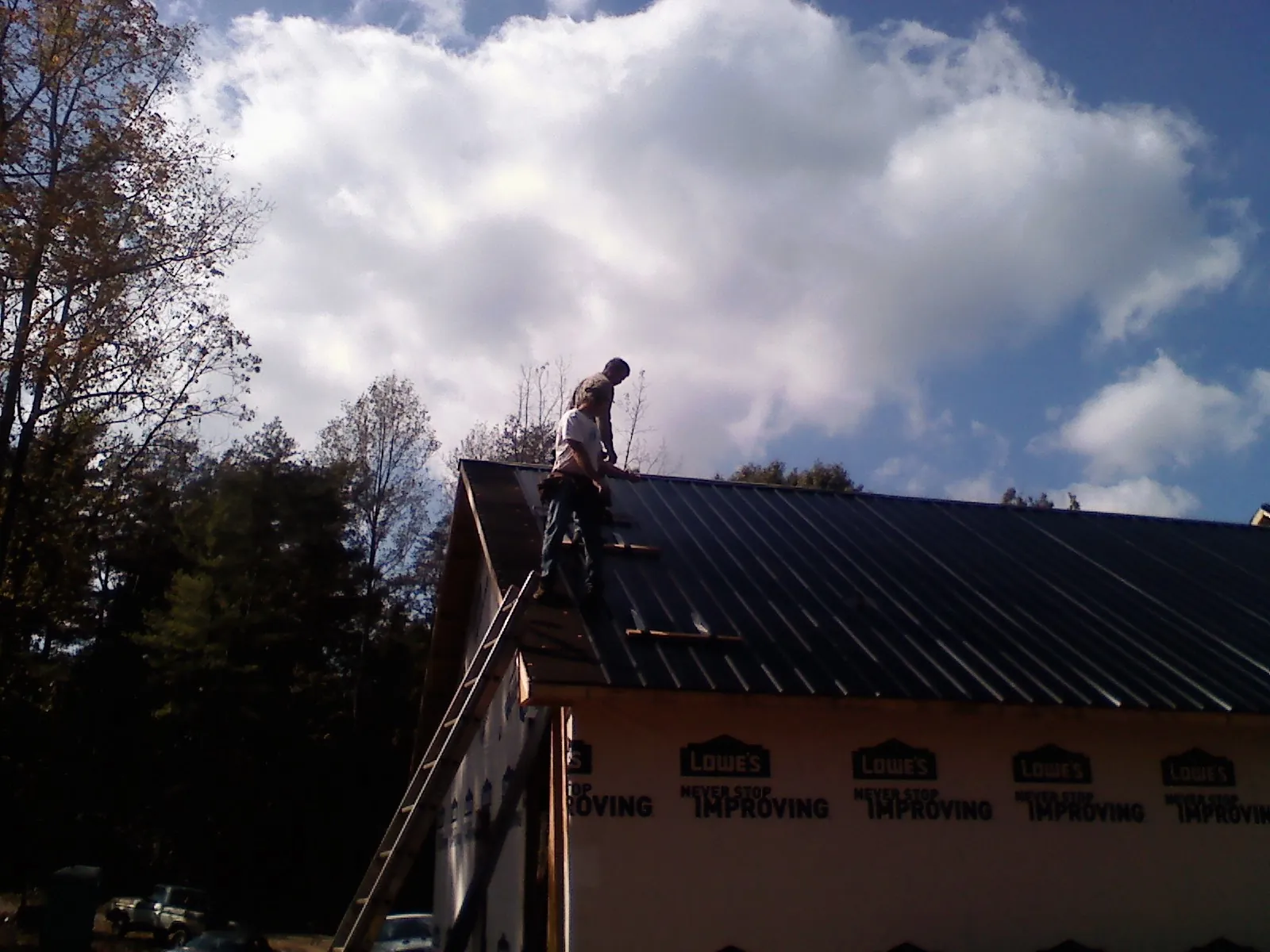 Roofer fastening dark metal panels high against a cloudy sky, from a Roof Inspection job in Fort Mc Coy