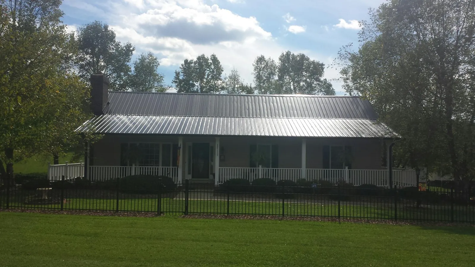Gray metal roof on a brick ranch with a full width front porch — Gutter Guard Installation work by our crew in Fort Mc Coy