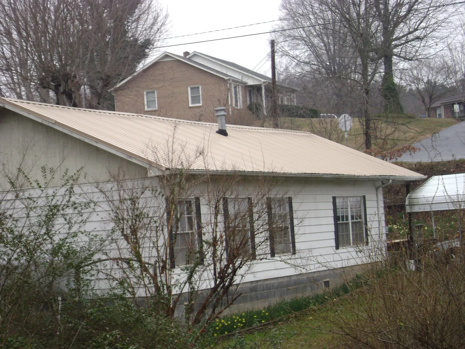 Tan metal roof on a white sided house set into a hillside — Commercial Roofing by Roofing Brothers in Fort Mc Coy