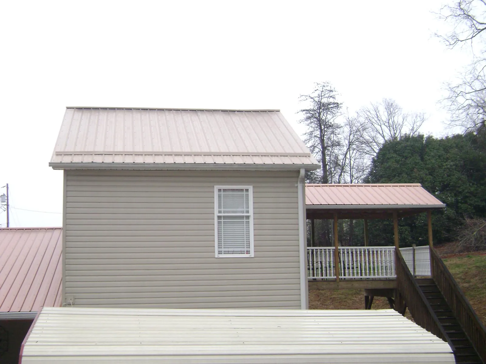 Tan metal roofs on a two story addition and attached porch, from a Roof Replacement job in Fort Mc Coy